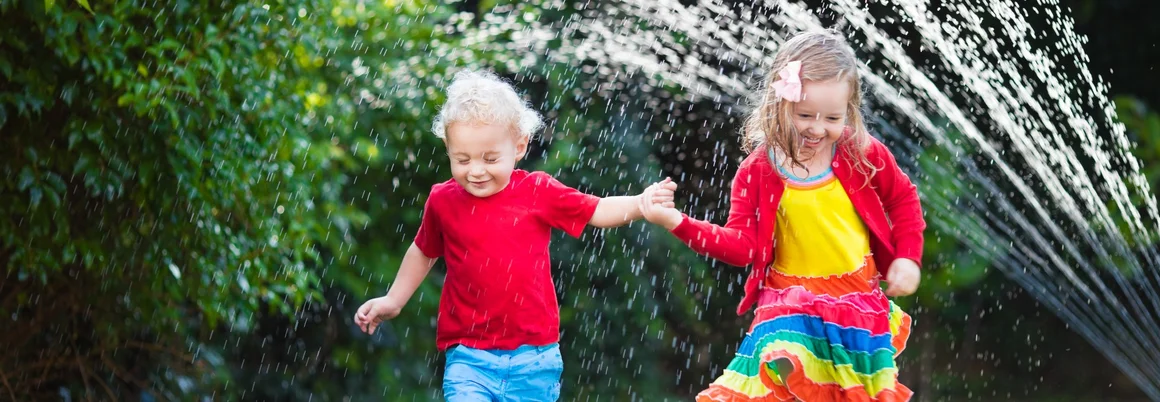 Zwei Kinder laufen unter einem Rasensprenger durch